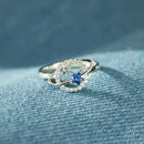 Delicado anel de prata com uma pedra preciosa azul cercada por pequenos diamantes em um design circular.