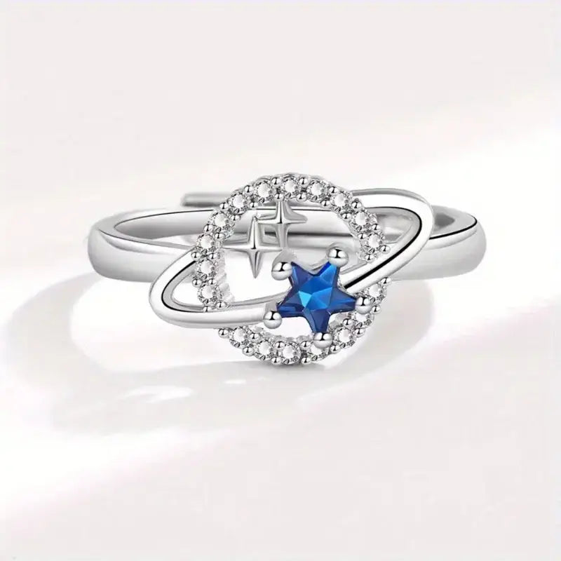Anel de prata com design semelhante a um planeta, com uma pedra preciosa azul em forma de estrela e detalhes em diamante.