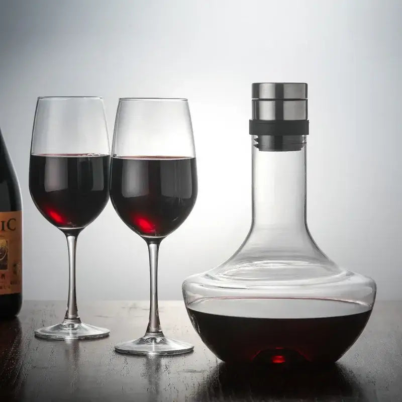 Decanter de vinho com base larga e gargalo estreito, acompanhado de duas taças de vinho cheias.