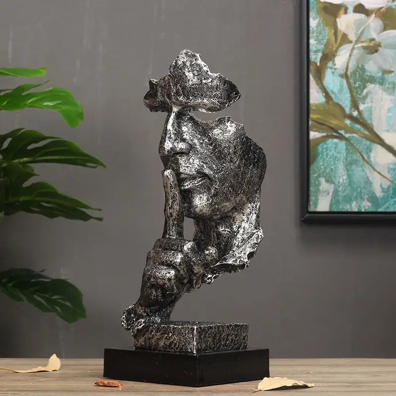 Escultura metálica de uma figura contemplativa com a mão no queixo em uma pose de pensamento.