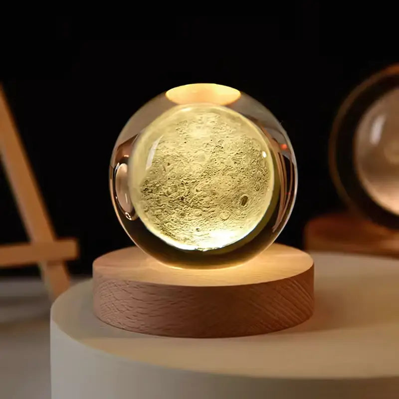 Esfera de vidro iluminada contendo uma superfície semelhante a uma lua em miniatura, apoiada em uma base de madeira.