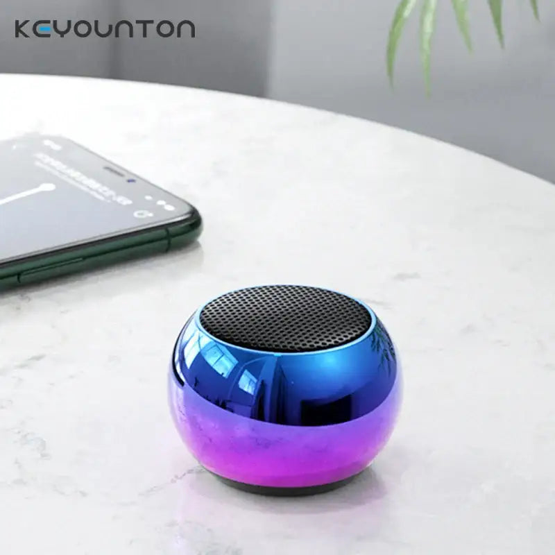Alto-falante Bluetooth esférico colorido com um acabamento metálico gradiente de azul a roxo.