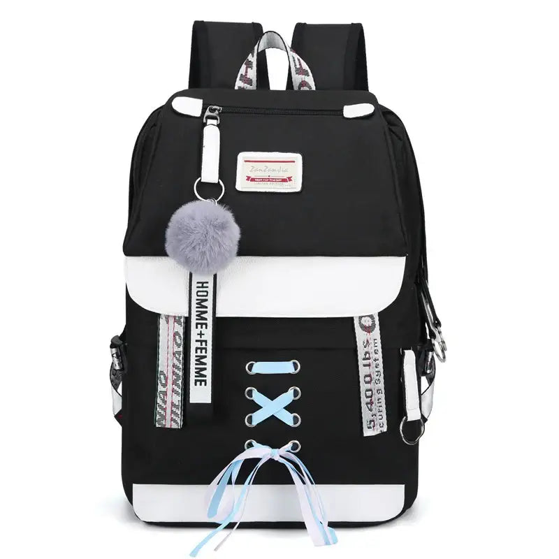 Mochila preta e branca com elementos decorativos, como um charme de pompom e detalhes em cadarço.