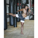 Homem musculoso sem camisa executando um chute alto em um ambiente de academia.