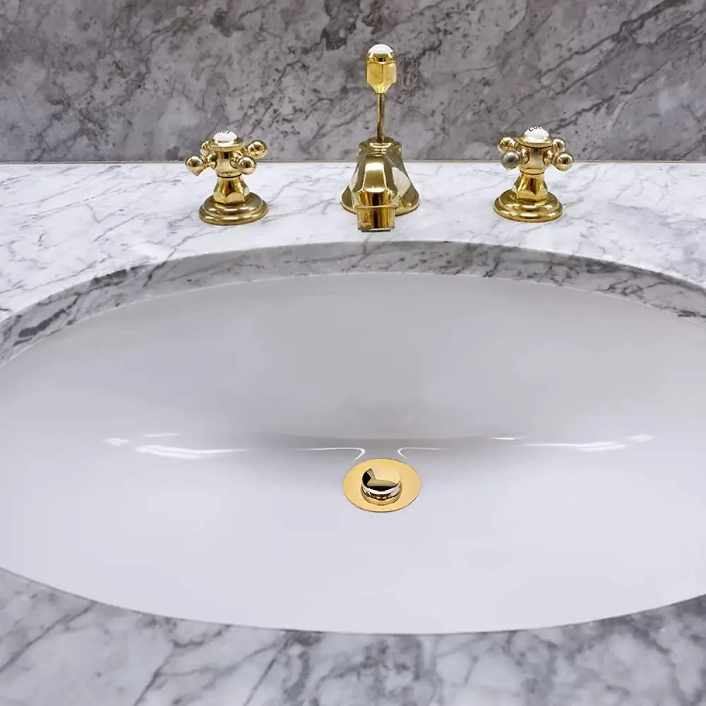 Pia oval de cerâmica branca com torneiras banhadas a ouro.