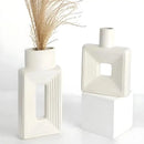 Vasos geométricos modernos de cerâmica branca com aberturas retangulares e desenhos concêntricos com sulcos.